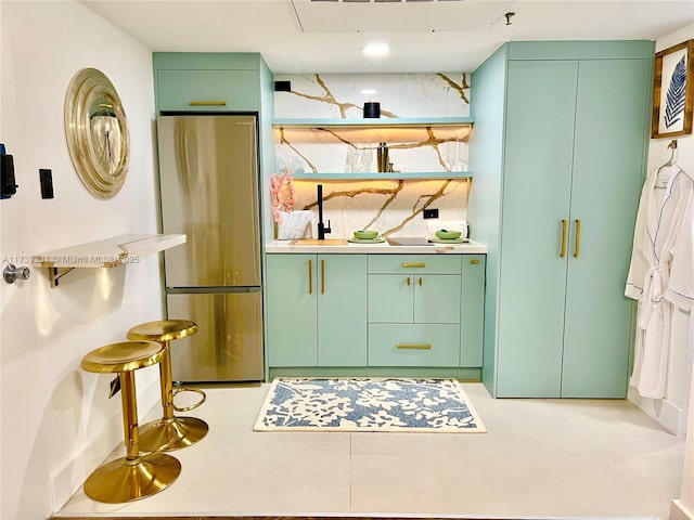 bar with green cabinets, stainless steel fridge, and decorative backsplash