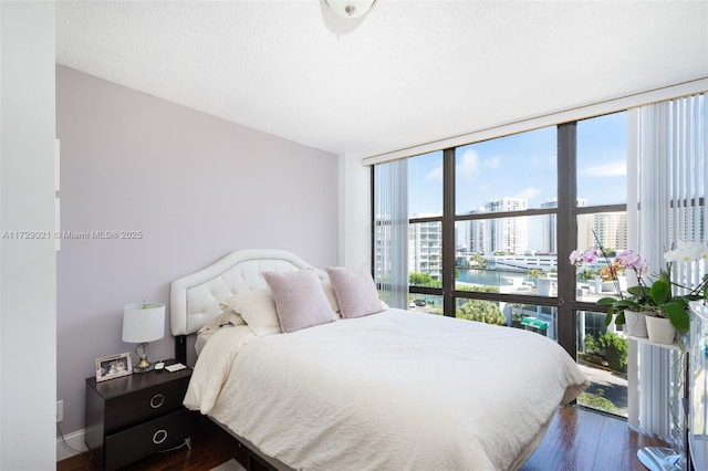 bedroom with dark hardwood / wood-style flooring, a wall of windows, a textured ceiling, and a water view