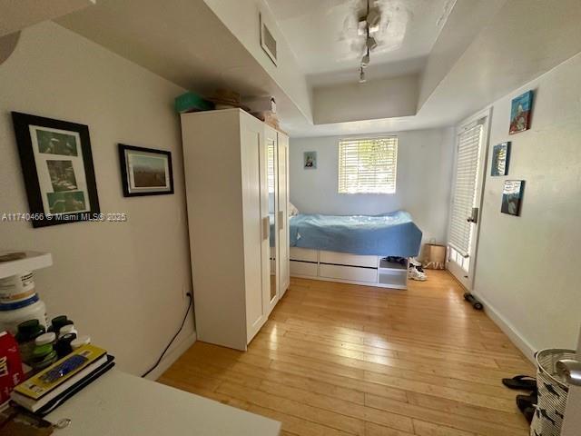 bedroom featuring rail lighting, light hardwood / wood-style floors, and a raised ceiling