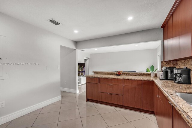 kitchen with light tile patterned flooring, backsplash, light stone counters, and kitchen peninsula