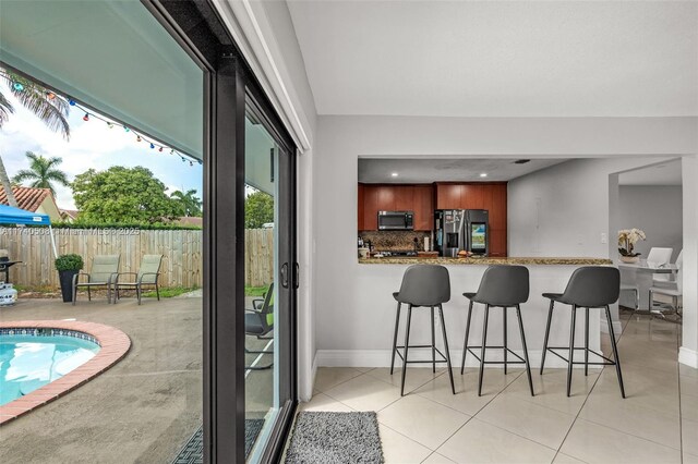 interior space with light tile patterned floors, appliances with stainless steel finishes, light stone counters, decorative backsplash, and kitchen peninsula