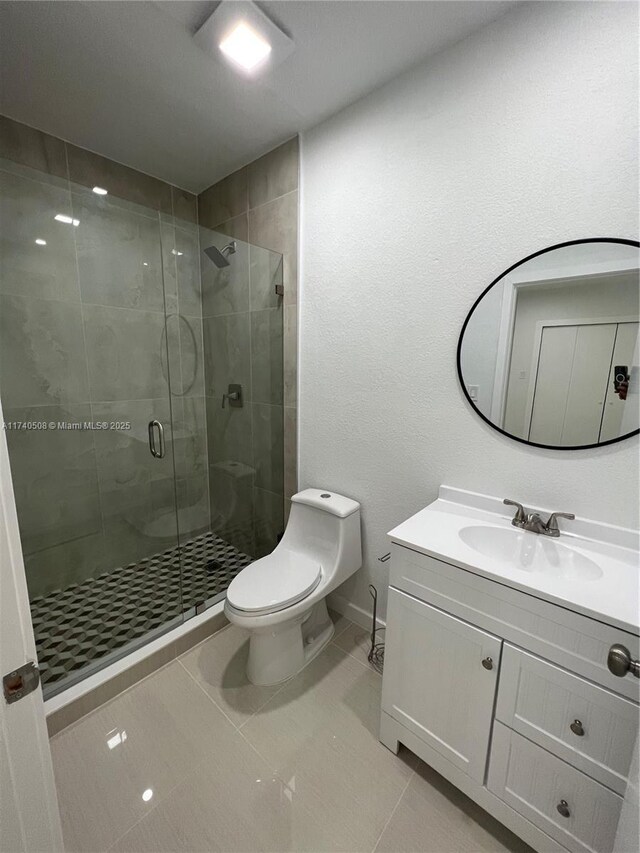 bathroom with a shower with door, vanity, tile patterned floors, and toilet