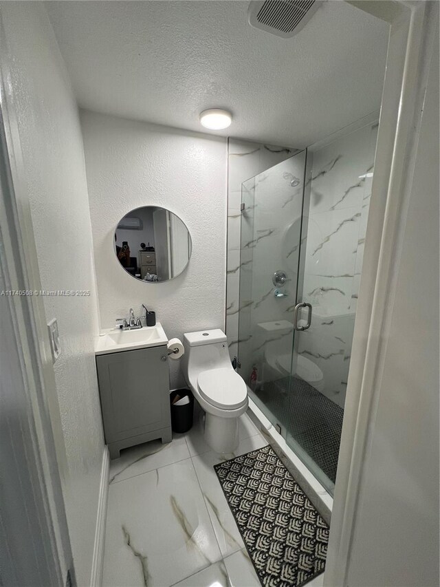 bathroom with vanity, toilet, a shower with door, and a textured ceiling