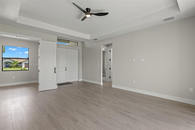 unfurnished bedroom featuring ceiling fan, a raised ceiling, and light hardwood / wood-style floors