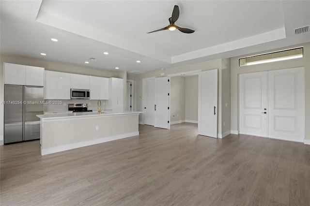 kitchen featuring stainless steel appliances, a center island with sink, white cabinets, and a tray ceiling