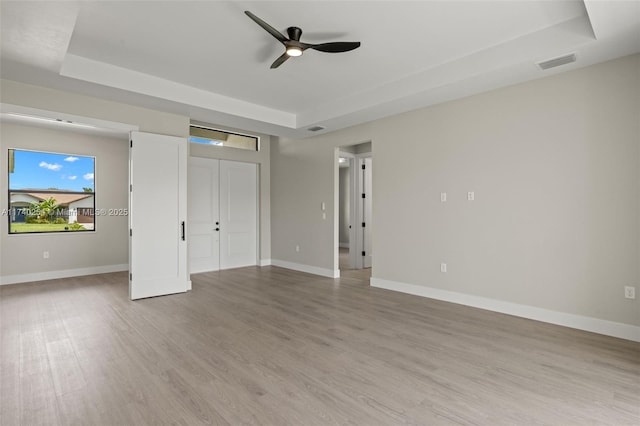 unfurnished bedroom with ceiling fan, a tray ceiling, and light hardwood / wood-style flooring