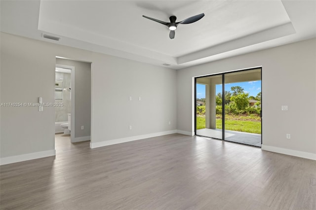 empty room featuring ceiling fan, wood-type flooring, and a raised ceiling