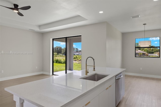 kitchen with sink, hanging light fixtures, light stone counters, white cabinets, and a center island with sink