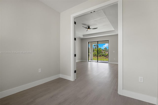 unfurnished room featuring a raised ceiling, wood-type flooring, and ceiling fan