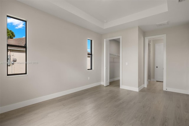 unfurnished bedroom with a walk in closet, a tray ceiling, light hardwood / wood-style flooring, and a closet