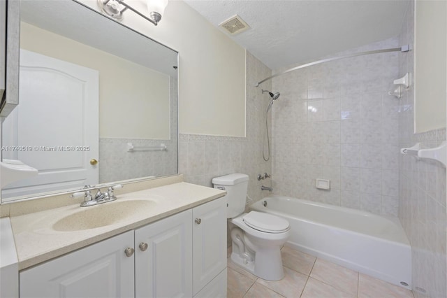 full bathroom featuring tile patterned flooring, tile walls, tiled shower / bath combo, vanity, and a textured ceiling