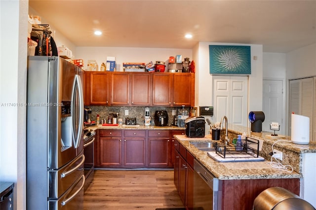 kitchen featuring sink, decorative backsplash, light stone counters, stainless steel appliances, and light wood-type flooring