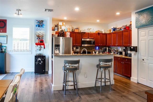 kitchen with a breakfast bar, a center island with sink, stainless steel appliances, dark hardwood / wood-style floors, and stone countertops