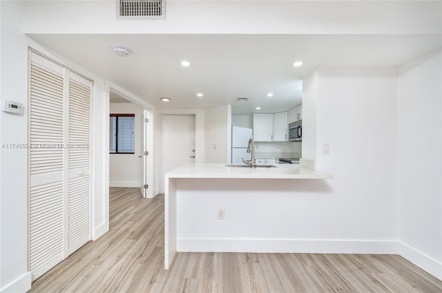 kitchen with white cabinetry, sink, white refrigerator, light hardwood / wood-style floors, and kitchen peninsula