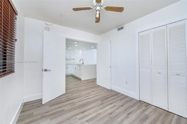 unfurnished bedroom featuring sink, a textured ceiling, light hardwood / wood-style floors, and a closet