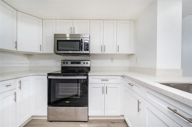 kitchen with light stone counters, light hardwood / wood-style flooring, white cabinets, and appliances with stainless steel finishes