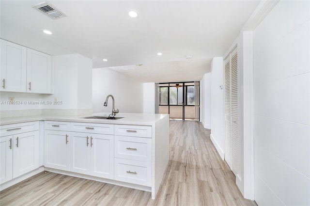 kitchen with sink, light hardwood / wood-style floors, kitchen peninsula, and white cabinets