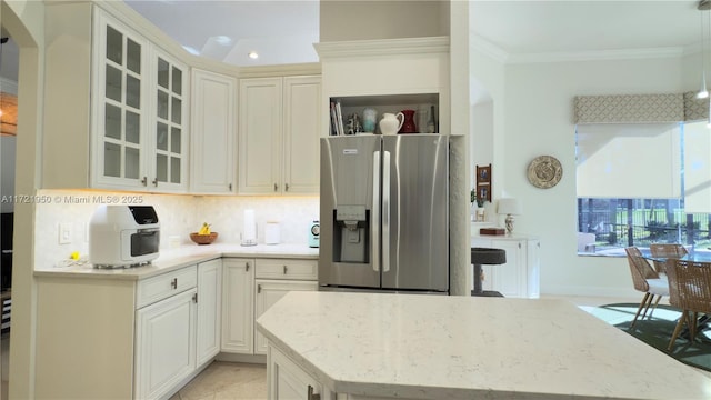 kitchen with crown molding, stainless steel fridge, pendant lighting, light stone countertops, and backsplash