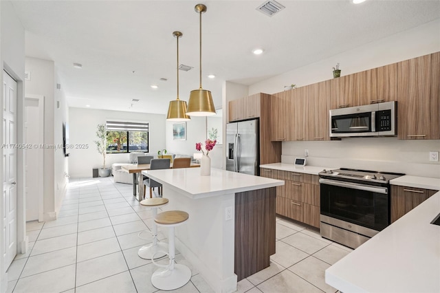 kitchen with light tile patterned floors, a breakfast bar area, hanging light fixtures, stainless steel appliances, and a center island