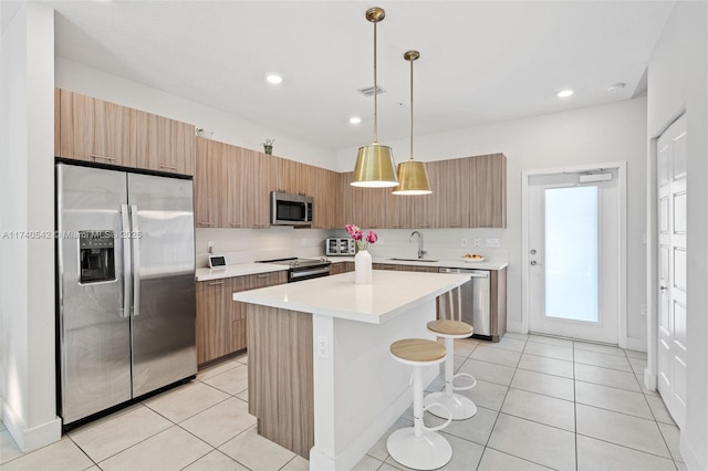 kitchen featuring light tile patterned floors, sink, hanging light fixtures, stainless steel appliances, and a kitchen island