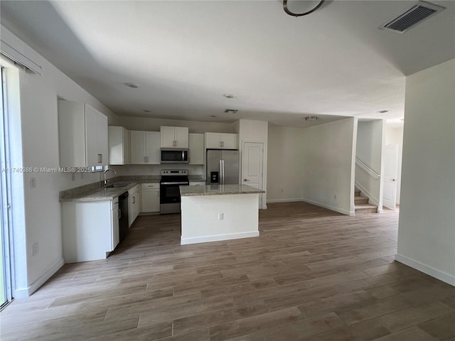 kitchen featuring sink, a center island, appliances with stainless steel finishes, light hardwood / wood-style floors, and white cabinets