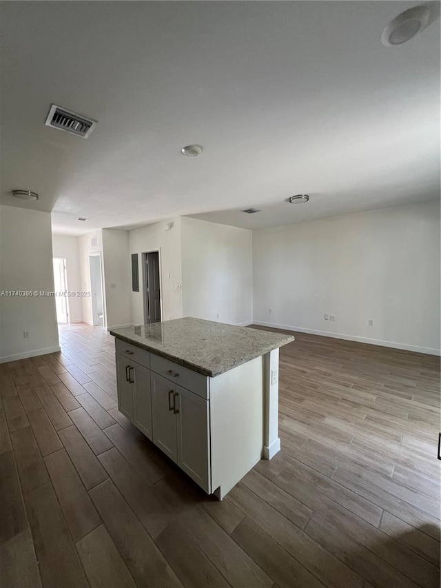 kitchen with light stone countertops, light hardwood / wood-style floors, a kitchen island, and white cabinets