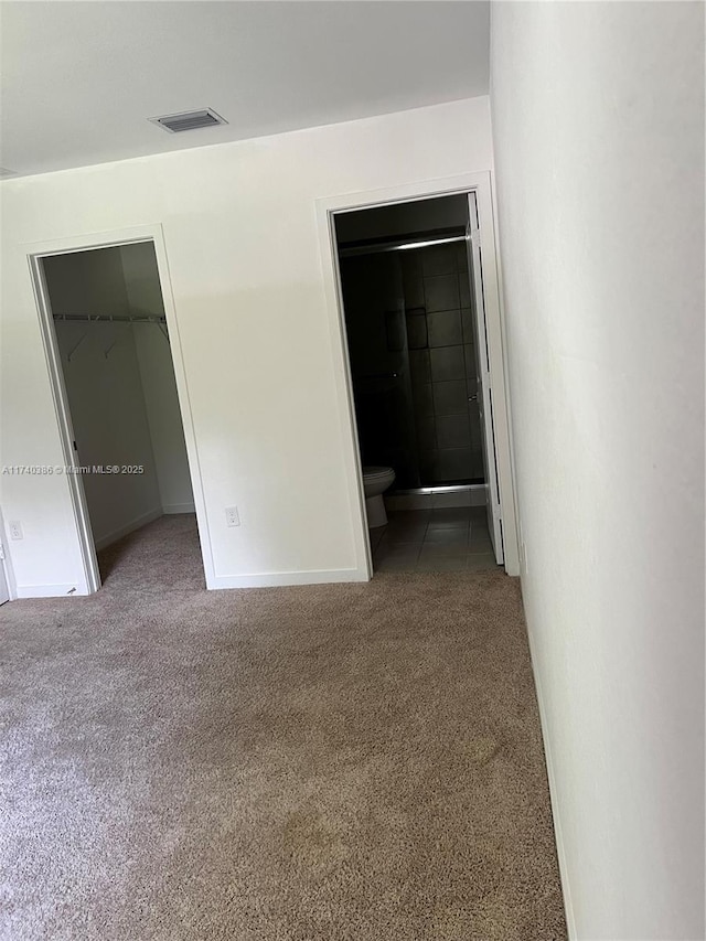 interior space featuring ensuite bathroom, a walk in closet, carpet floors, and a closet