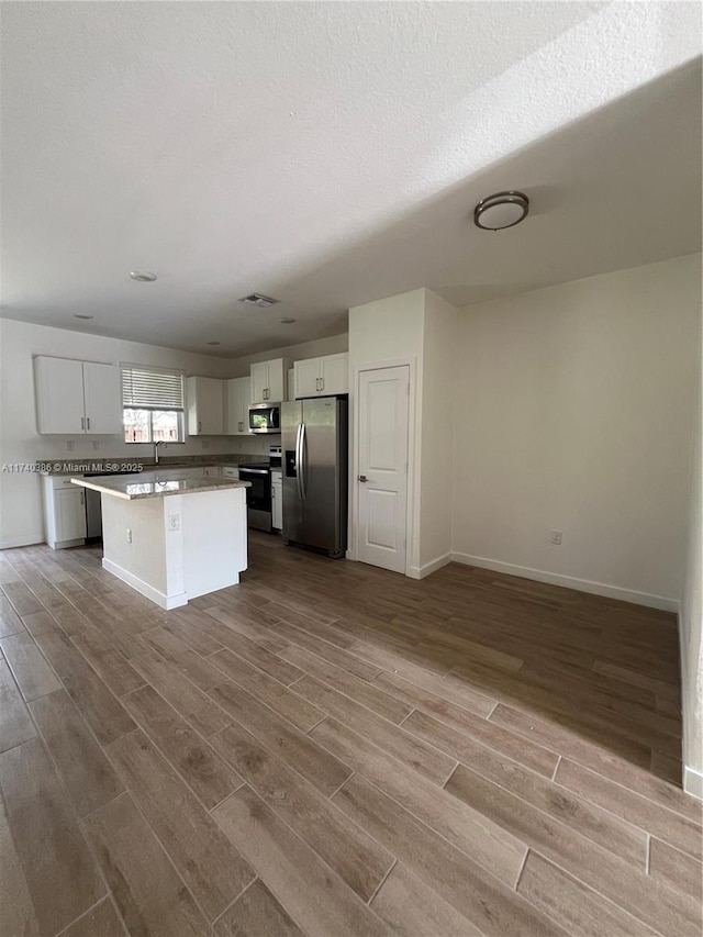 kitchen with a kitchen island, appliances with stainless steel finishes, white cabinets, and light hardwood / wood-style floors