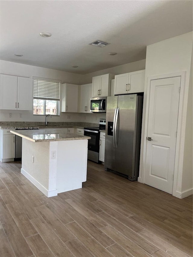 kitchen featuring sink, appliances with stainless steel finishes, a kitchen island, light hardwood / wood-style floors, and white cabinets