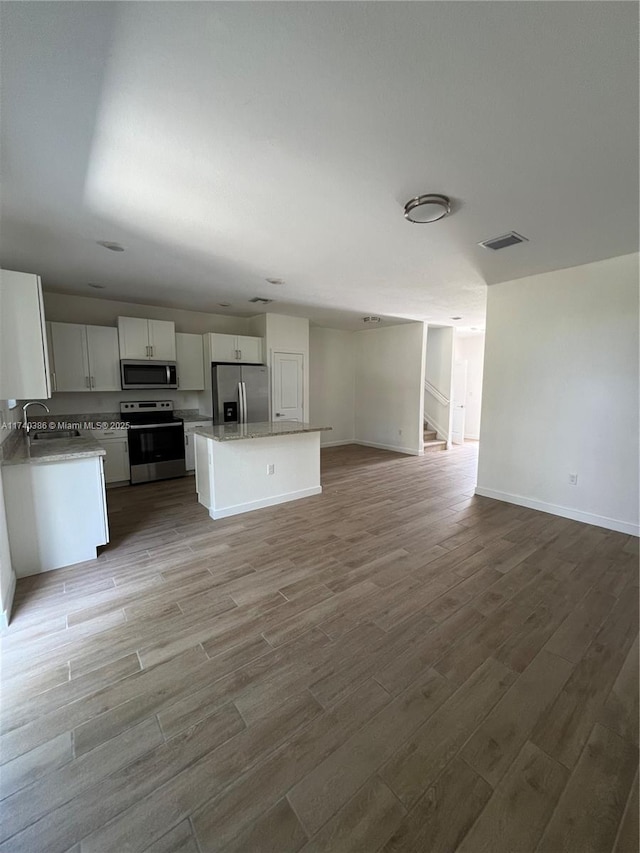 kitchen with sink, appliances with stainless steel finishes, a center island, wood-type flooring, and white cabinets