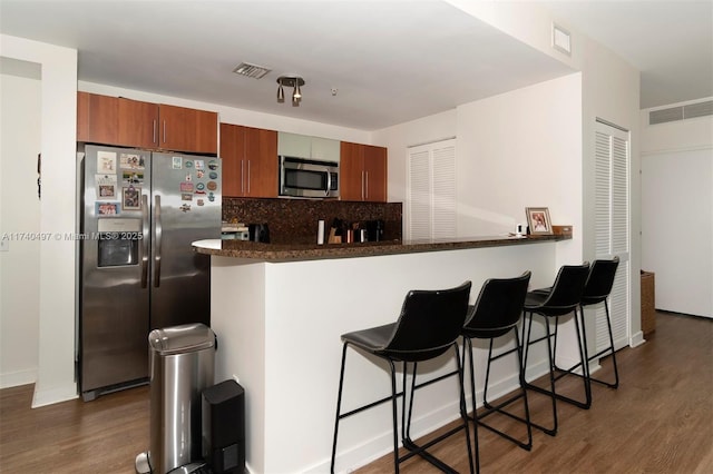 kitchen featuring dark hardwood / wood-style flooring, appliances with stainless steel finishes, a kitchen breakfast bar, and kitchen peninsula