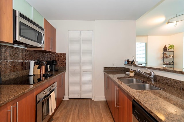 kitchen with sink, appliances with stainless steel finishes, dark stone countertops, hardwood / wood-style floors, and tasteful backsplash