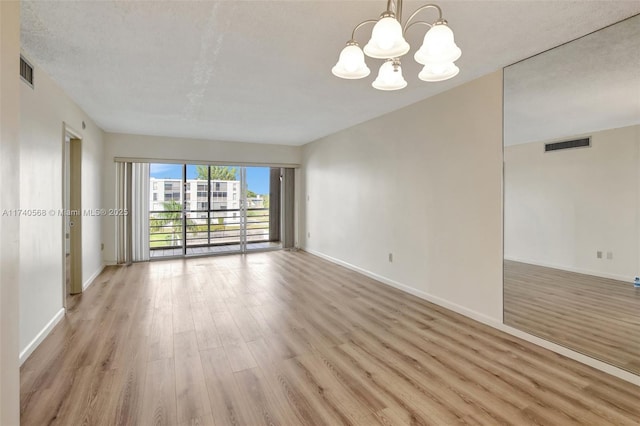 unfurnished room with a textured ceiling, a notable chandelier, and light hardwood / wood-style floors