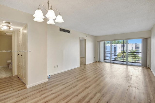 spare room featuring a chandelier, a textured ceiling, and light hardwood / wood-style floors