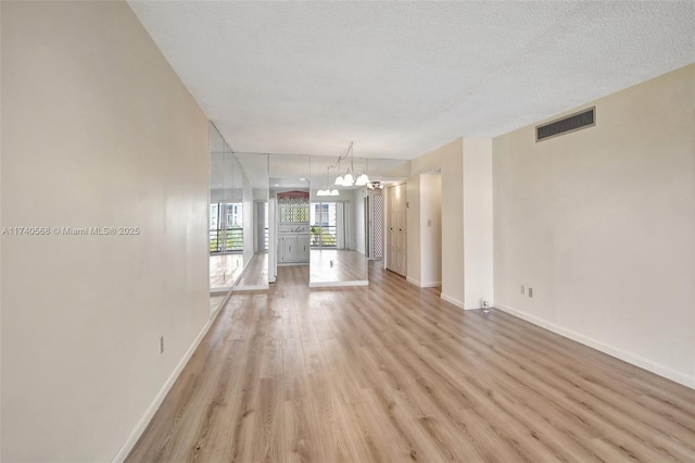 unfurnished living room with an inviting chandelier, a textured ceiling, and light wood-type flooring