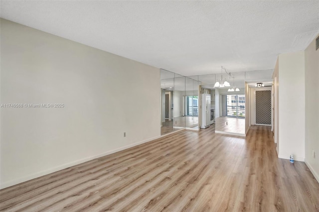 unfurnished living room with an inviting chandelier, a textured ceiling, and light wood-type flooring