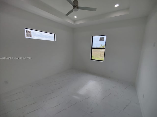 spare room featuring ceiling fan, a tray ceiling, and a healthy amount of sunlight