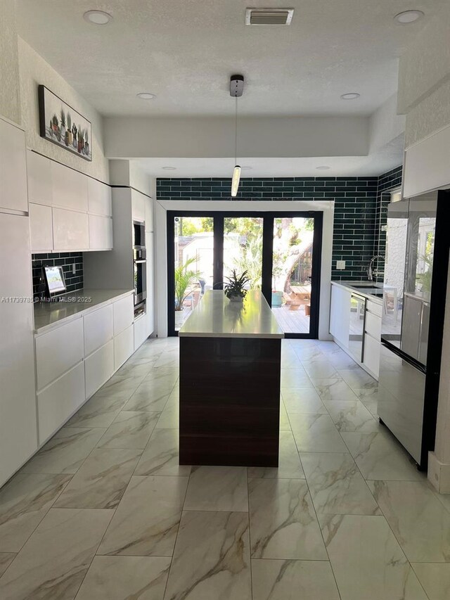 kitchen featuring decorative light fixtures, dishwasher, a kitchen island, white cabinets, and backsplash