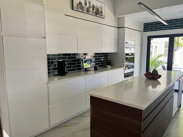 kitchen with a center island, dark brown cabinets, white cabinets, light stone countertops, and backsplash