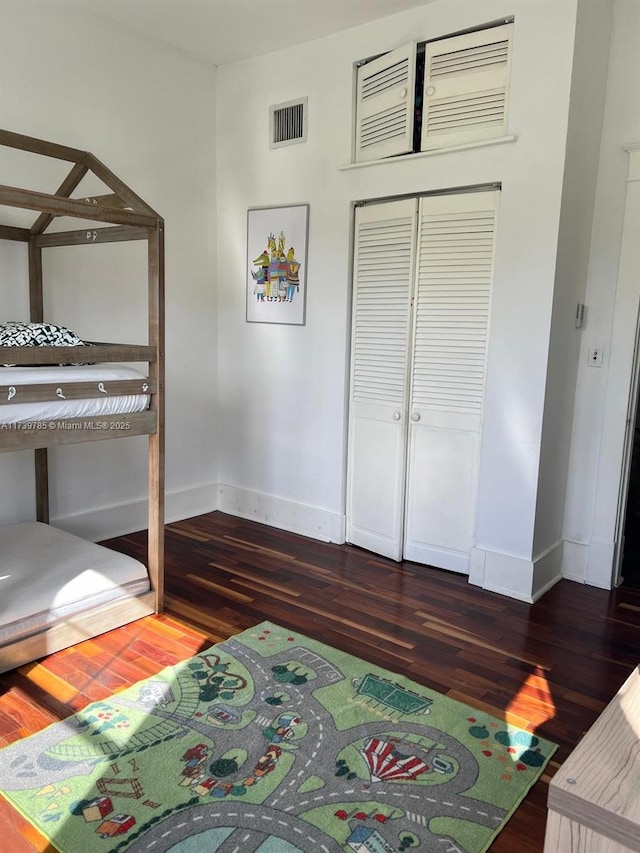 unfurnished bedroom with dark wood-style floors, baseboards, visible vents, and a closet