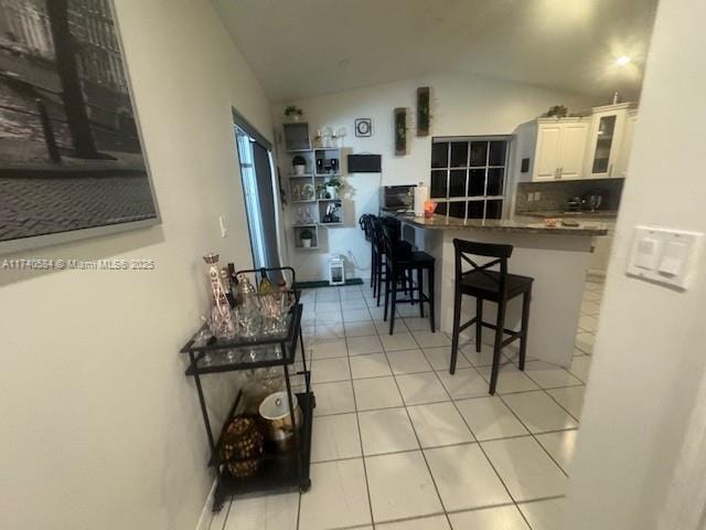 kitchen featuring vaulted ceiling, white cabinetry, a kitchen breakfast bar, light tile patterned floors, and kitchen peninsula