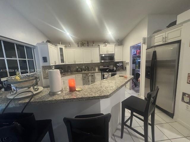 kitchen featuring vaulted ceiling, appliances with stainless steel finishes, light tile patterned flooring, tasteful backsplash, and white cabinets