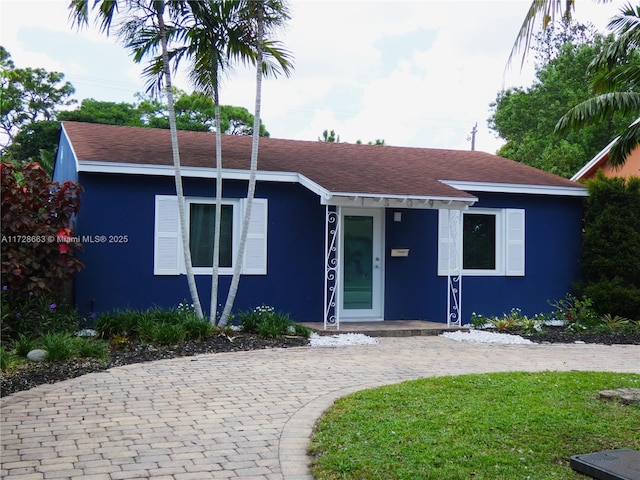 view of front of house featuring roof with shingles, a front lawn, and stucco siding