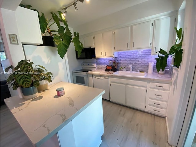 kitchen featuring light wood finished floors, white cabinets, a sink, white appliances, and a peninsula