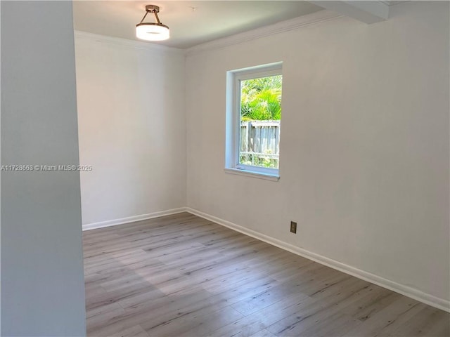 empty room with light wood-type flooring, baseboards, and crown molding