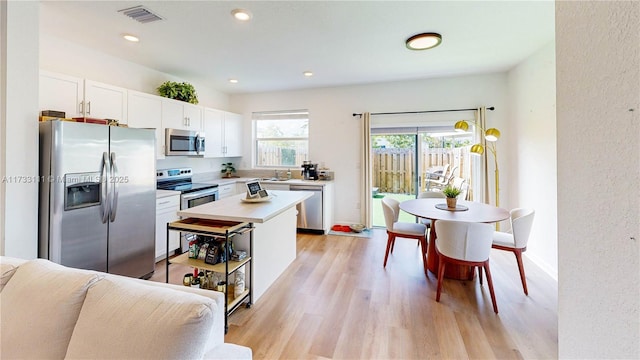 kitchen with sink, a center island, light wood-type flooring, appliances with stainless steel finishes, and white cabinets