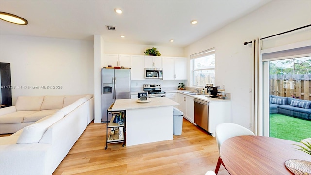 kitchen featuring appliances with stainless steel finishes, a breakfast bar area, white cabinets, a center island, and light wood-type flooring