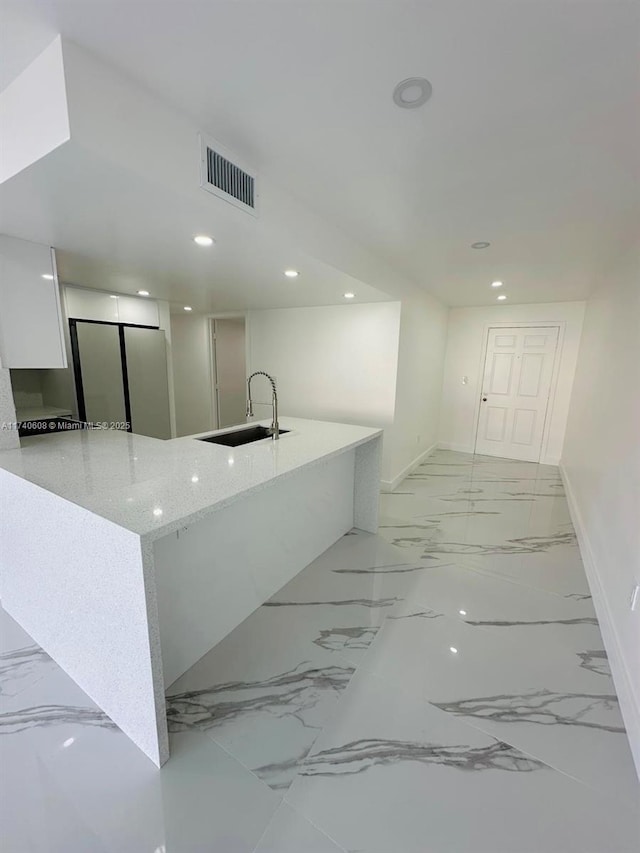 kitchen featuring sink, white cabinets, light stone counters, and kitchen peninsula