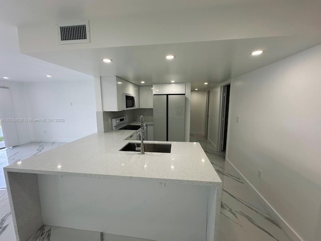 kitchen featuring white cabinetry, appliances with stainless steel finishes, kitchen peninsula, and light stone counters