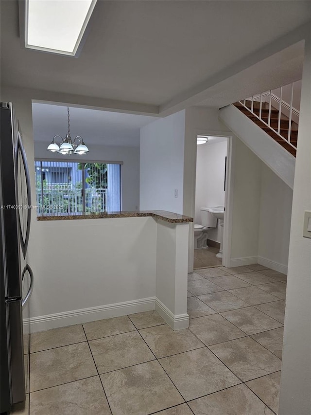 kitchen with an inviting chandelier, hanging light fixtures, light tile patterned floors, and stainless steel refrigerator